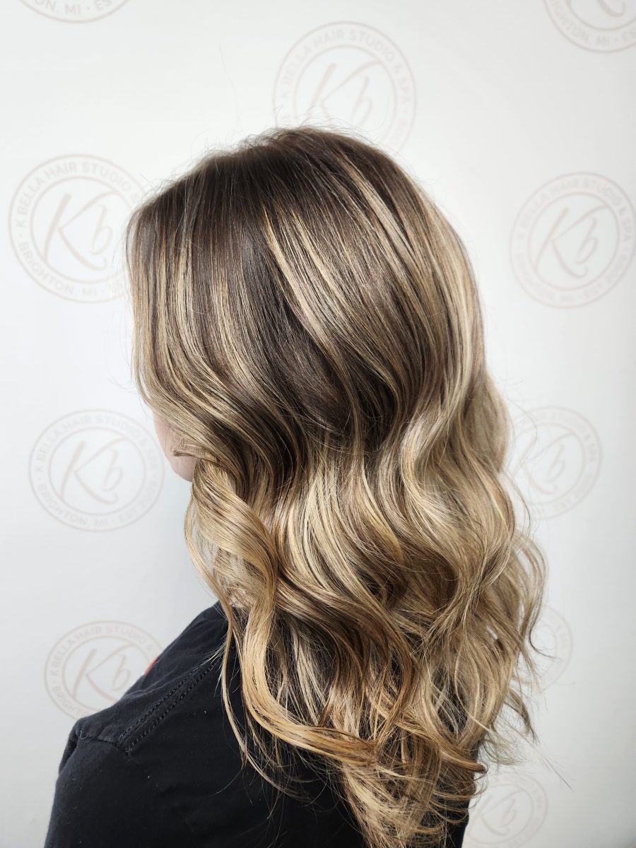 Side profile of long wavy hair with warm-toned balayage and softly textured layers by Siobhan Rozinski at K Bella Hair Studio & Spa in Brighton, MI