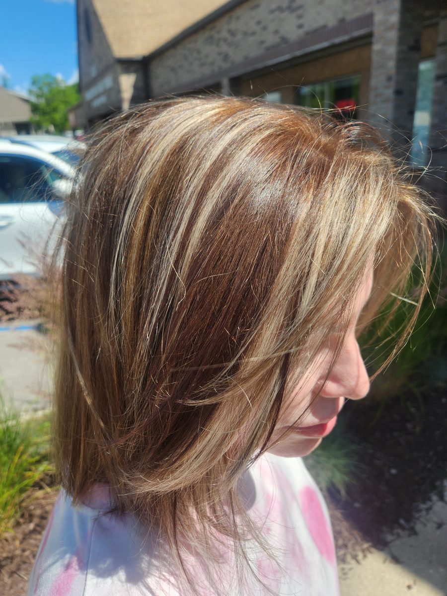 Side view of medium-length hair with warm caramel highlights blended into a medium brunette base in outdoor sunlight by Siobhan Rozinski at K Bella Hair Studio & Spa in Brighton, MI