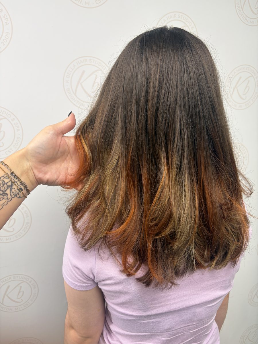 Rear view of shoulder-length layered hair with warm copper tones throughout, by Abbey French at K Bella Hair Studio & Spa in Brighton, MI