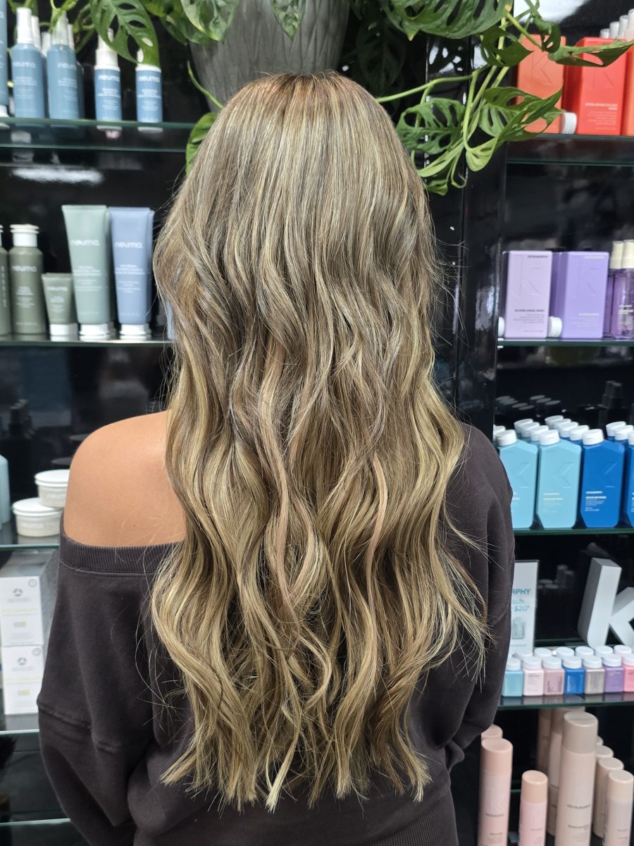 Long wavy hair with deep brunette tones and lighter balayage highlights, shown from behind, in a salon setting by Kristan Sayers at K Bella Hair Studio & Spa in Brighton, MI