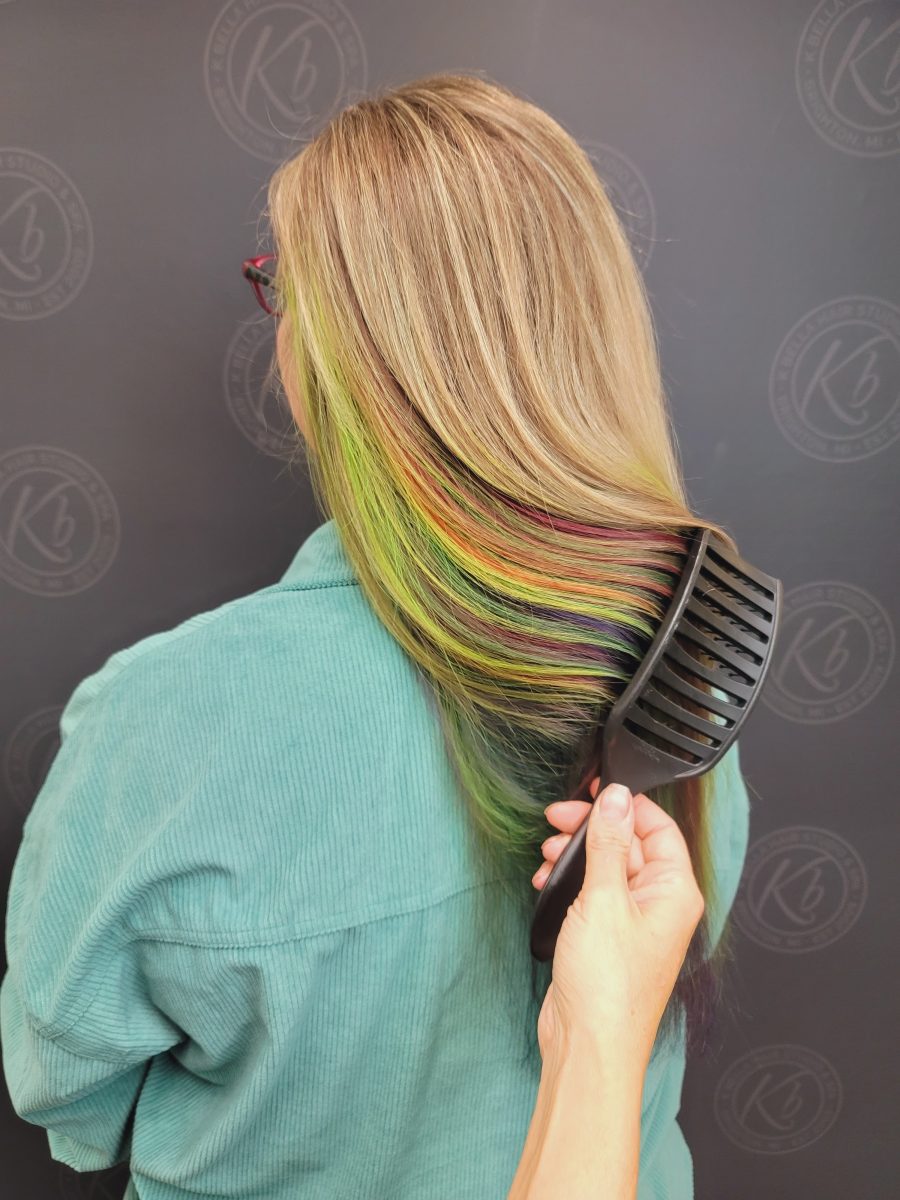 Back view of long blonde hair with rainbow colors melted through the layers by Kristan Sayers at K Bella Hair Studio & Spa in Brighton, MI