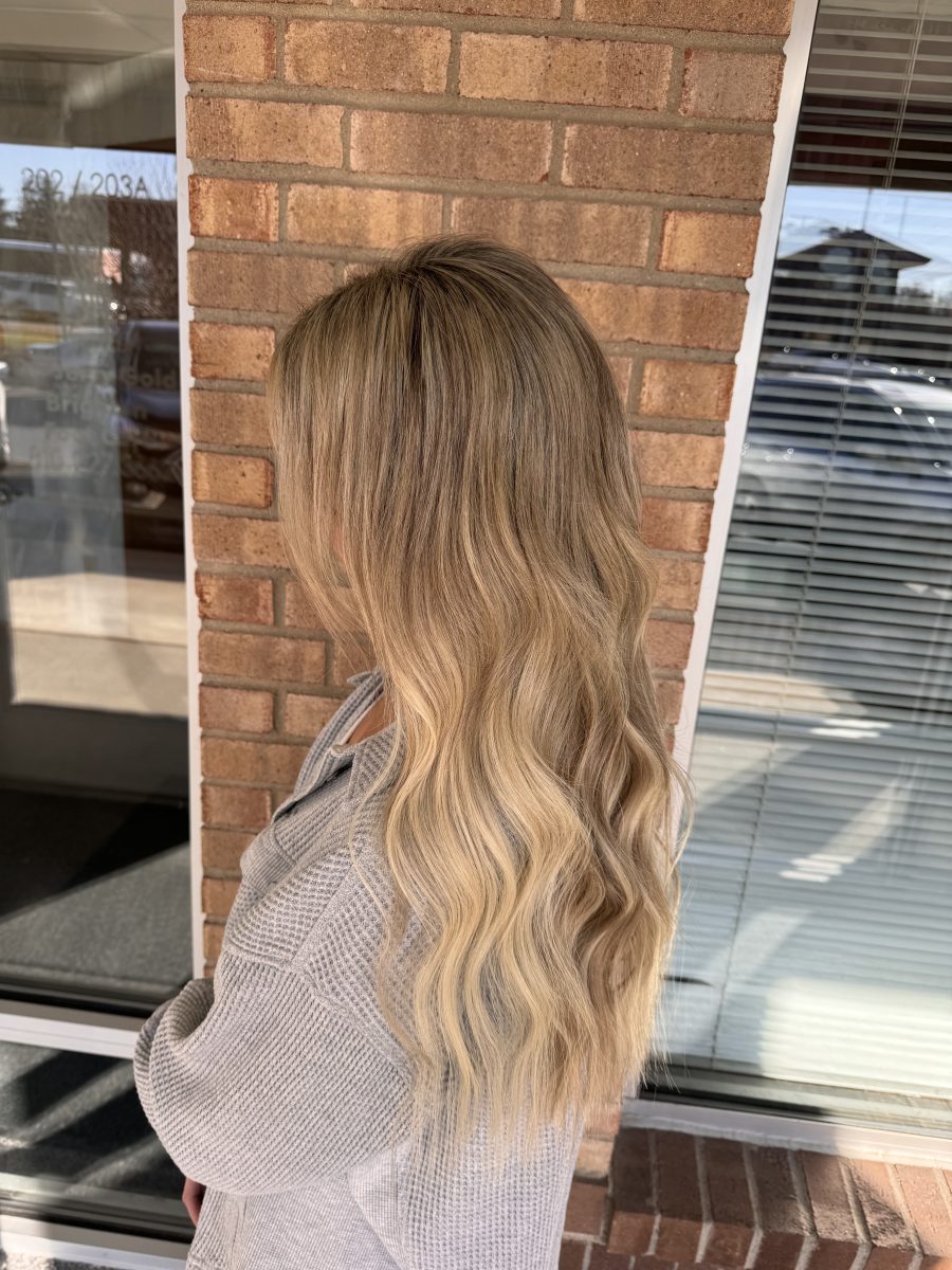 Rear view of long wavy hair with blonde highlights throughout, showing extension placement and texture, by Kristan Sayers at K Bella Hair Studio & Spa in Brighton, MI