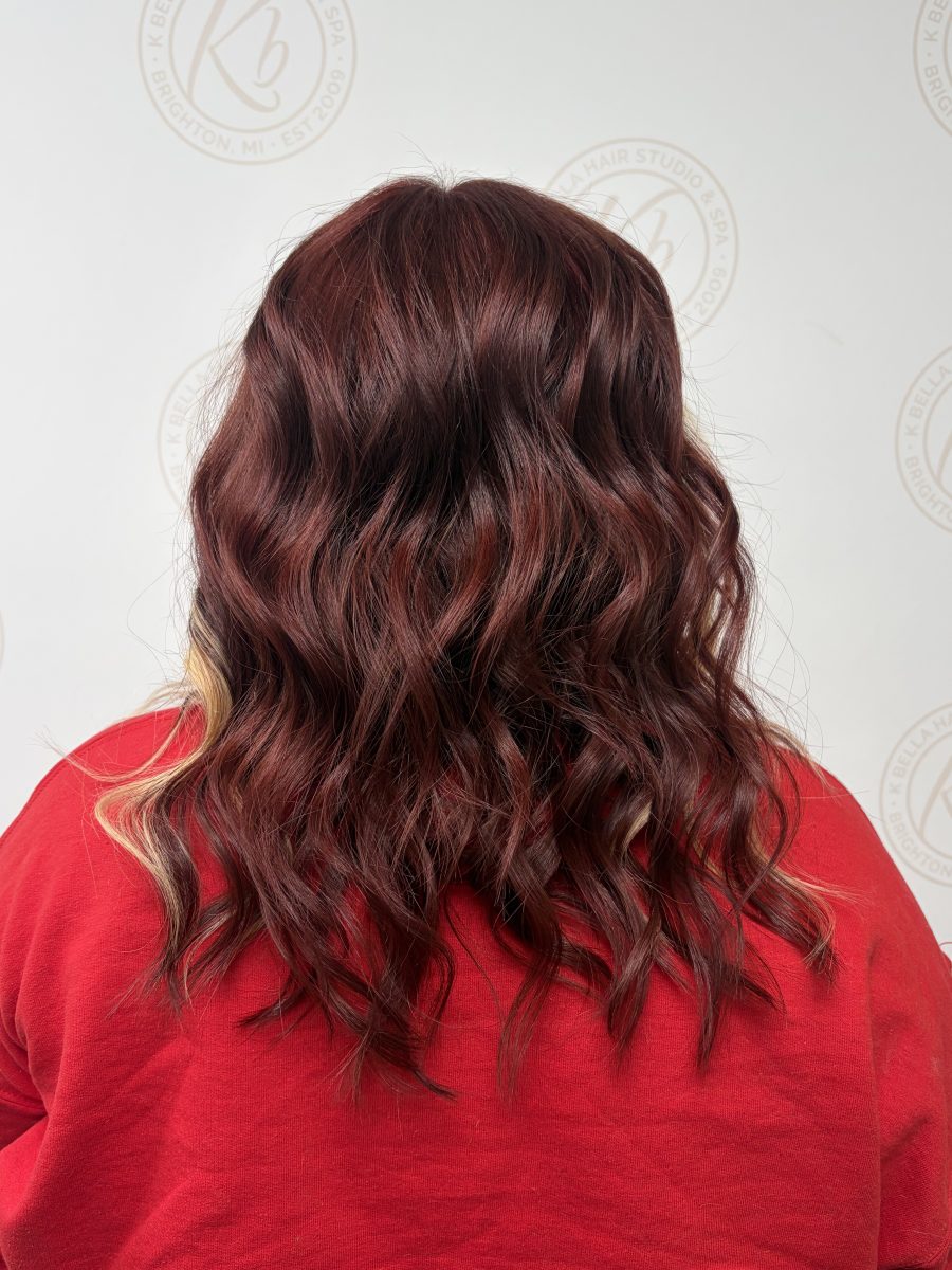 Back view of wavy burgundy hair with blonde woven through the waves by Abbey French at K Bella Hair Studio & Spa in Brighton, MI