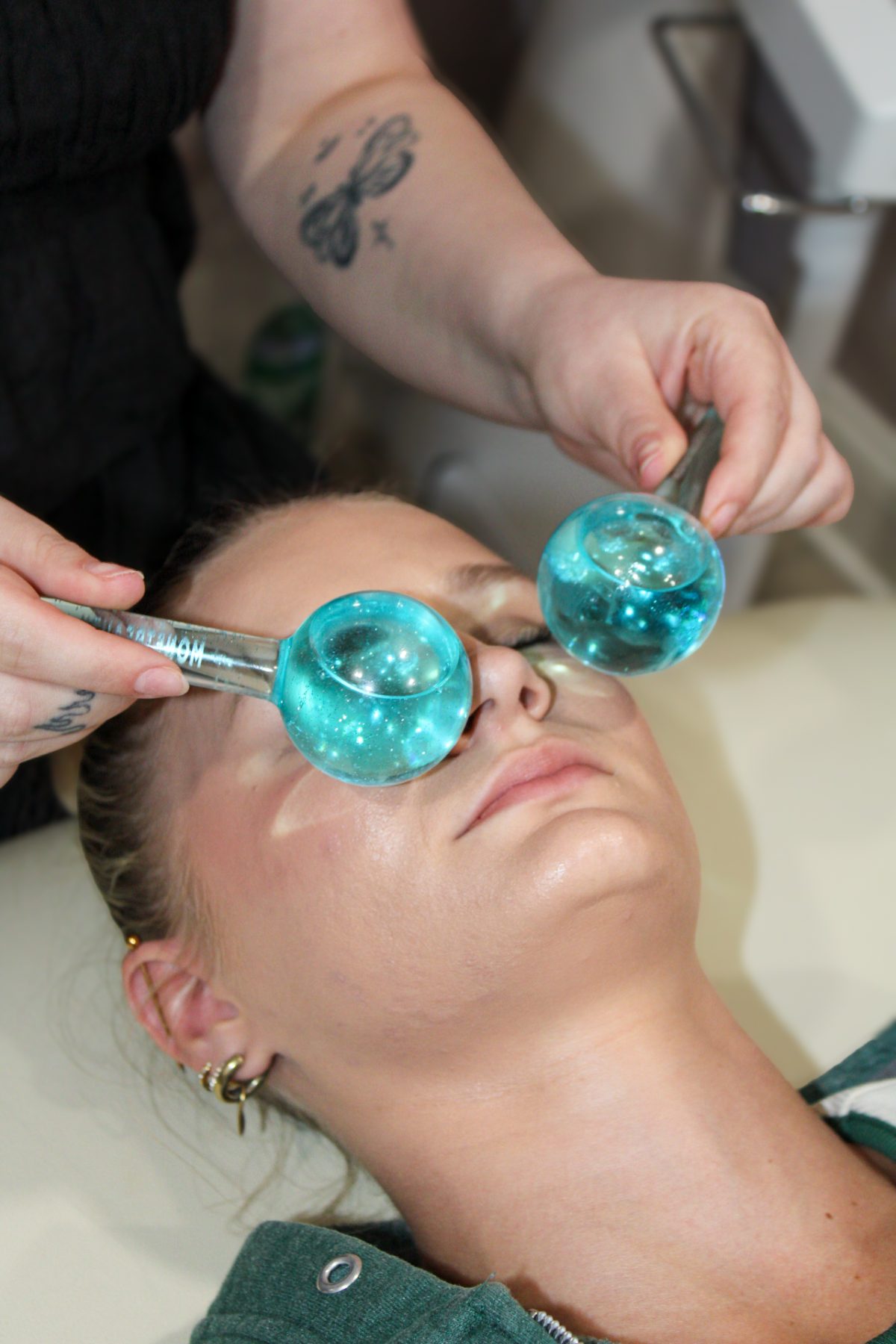 Esthetician gliding chilled cryo globes across a client's cheekbones during a facial at K Bella Hair Studio in Brighton, Michigan